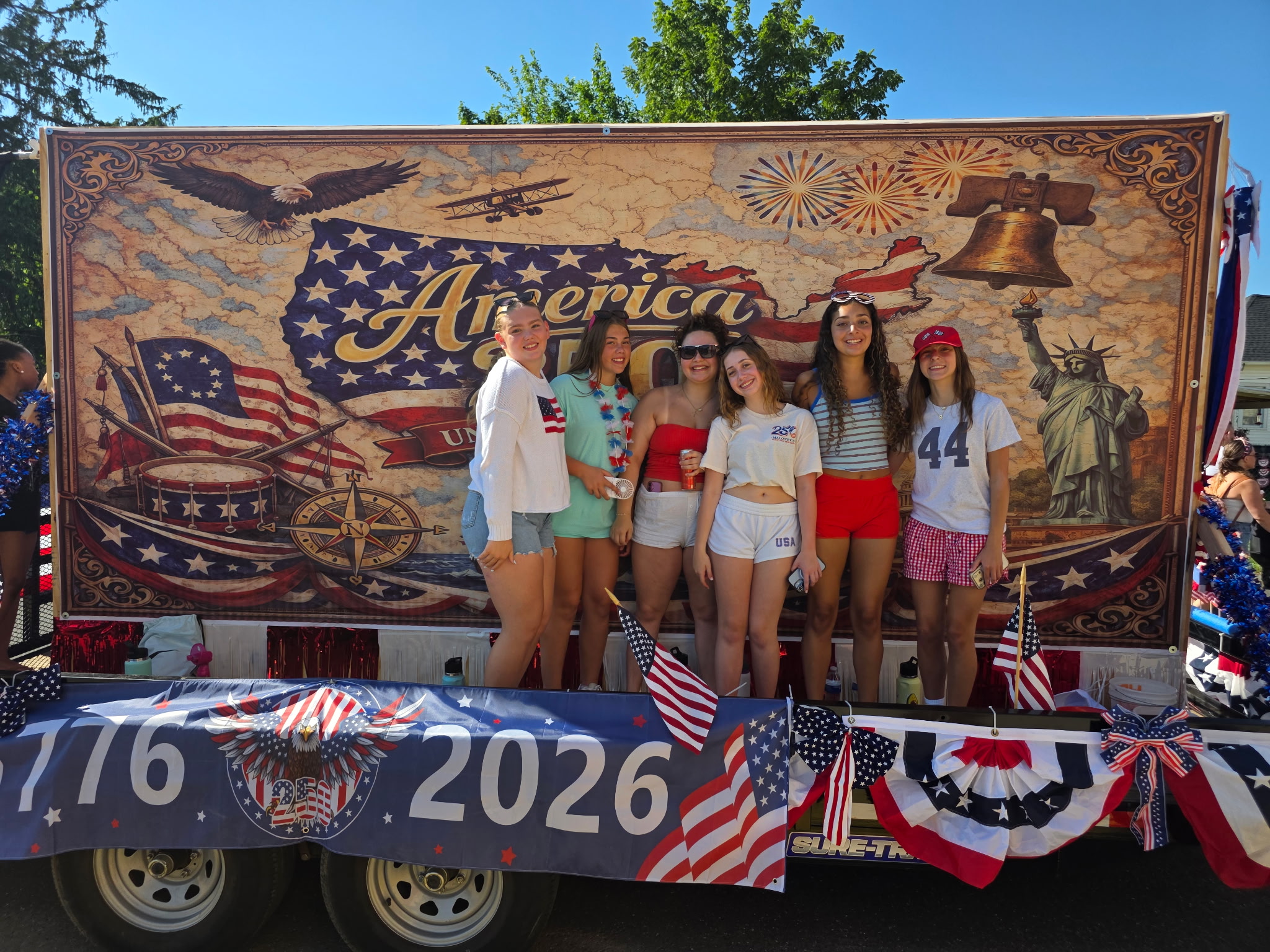 Six members of the Berlin community pose in front of the America 250 float — '1776 · 2026' banner, eagle, Liberty Bell, Statue of Liberty — Berlin NJ July 4th 2026