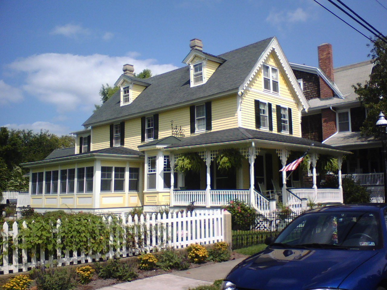 A yellow Victorian house with gingerbread trim, a wraparound porch and a white picket fence in Cape May