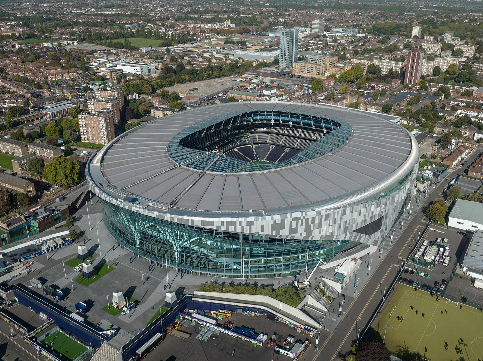 Aerial view of Tottenham Hotspur Stadium in north London, a large oval stadium with a silver and glass facade surrounded by houses