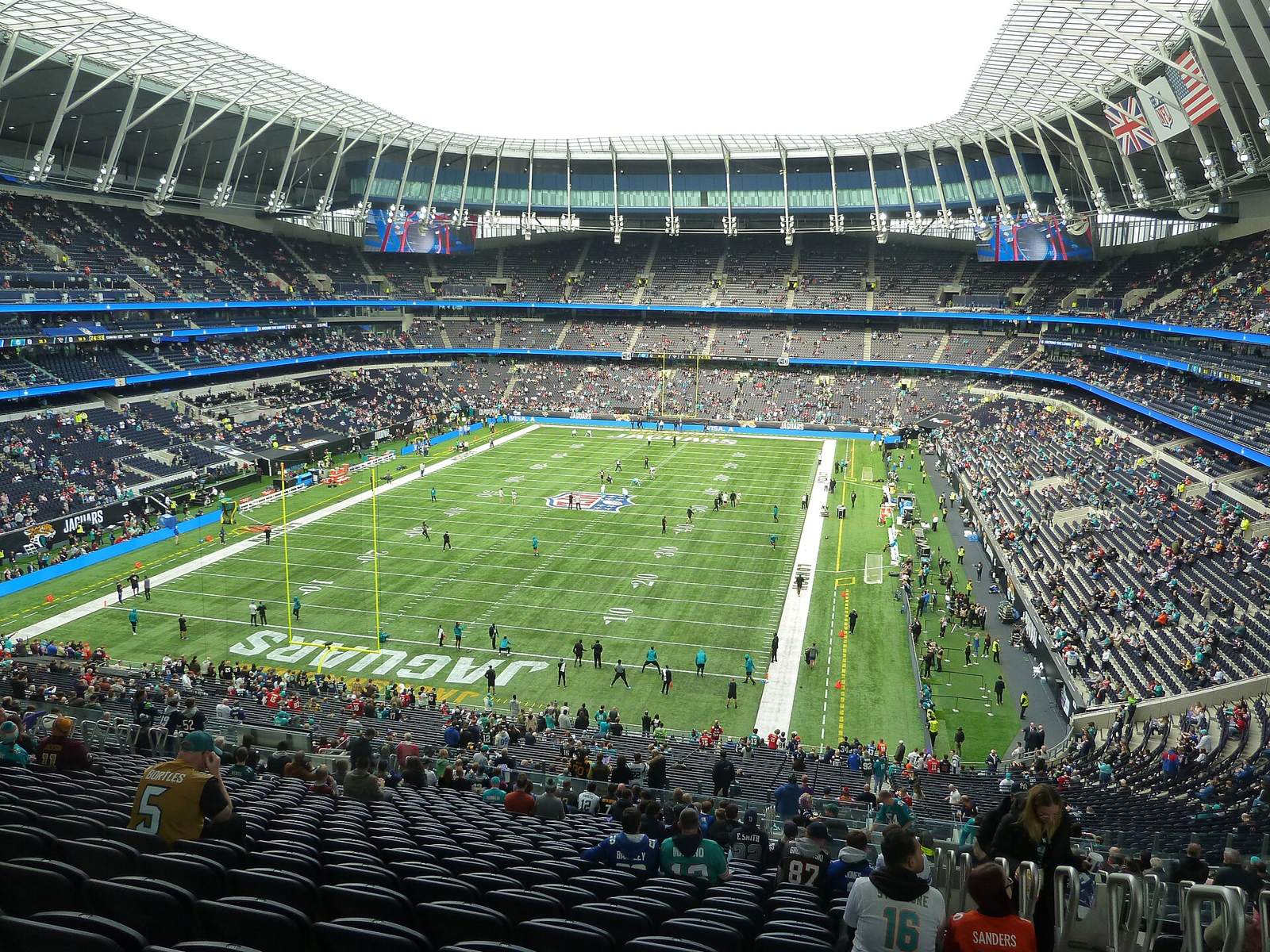 A football field with JAGUARS painted in the end zone inside Tottenham Hotspur Stadium, seen from the upper seats as fans arrive
