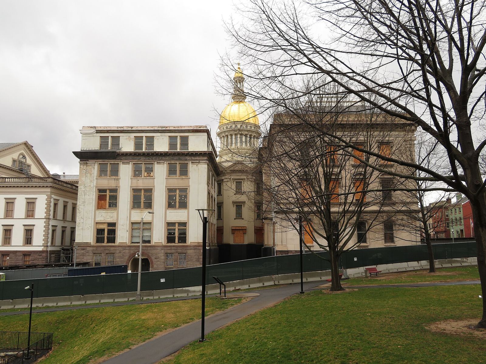 The gold dome of the New Jersey State House in Trenton rising behind older stone buildings and bare trees